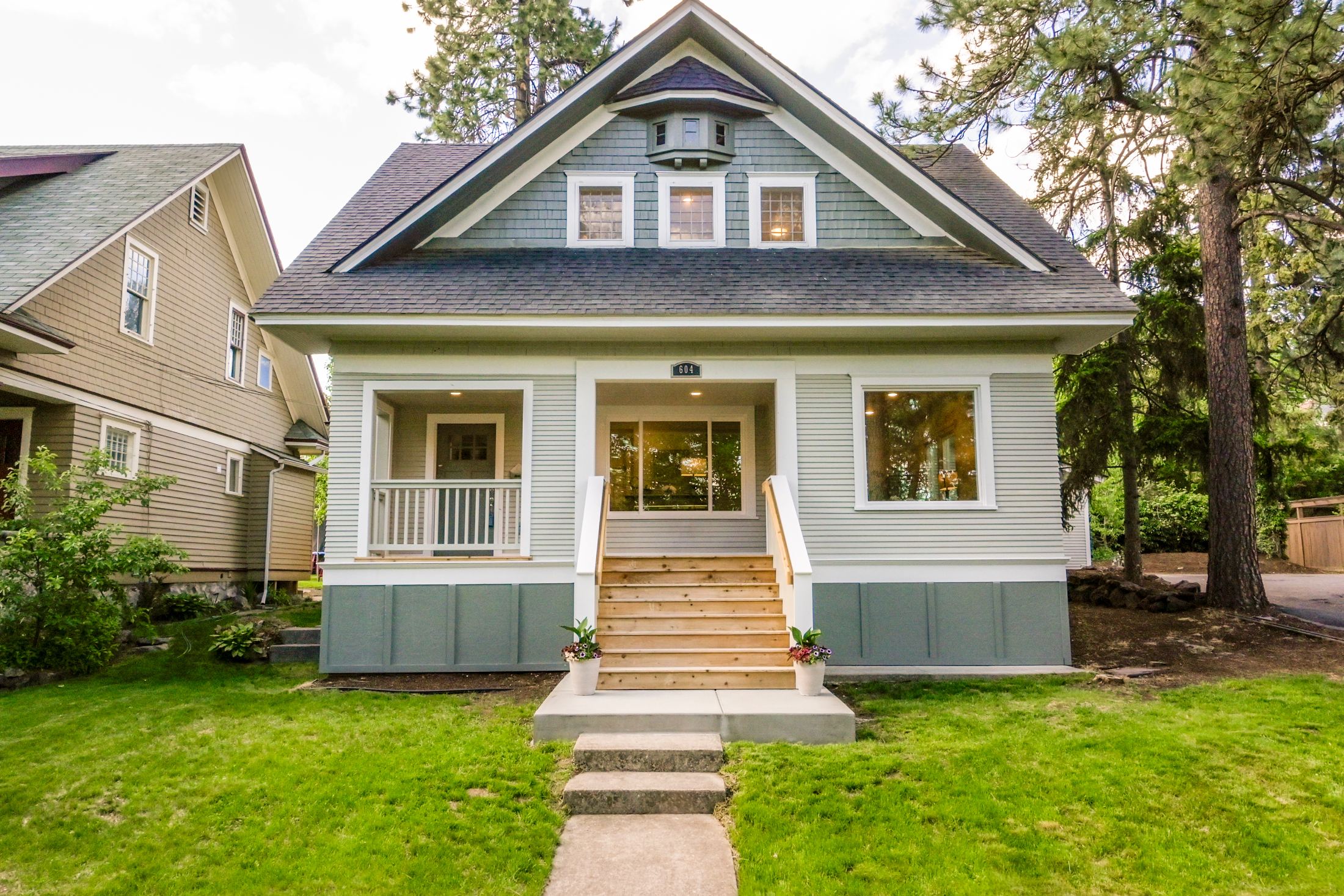Modern two-story house with white siding, covered porch, and landscaped front yard