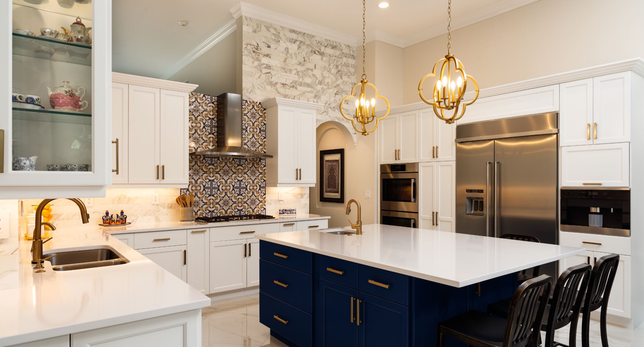 Luxury kitchen with white cabinetry, dark blue island, marble backsplash, stainless steel appliances and brass pendant lights