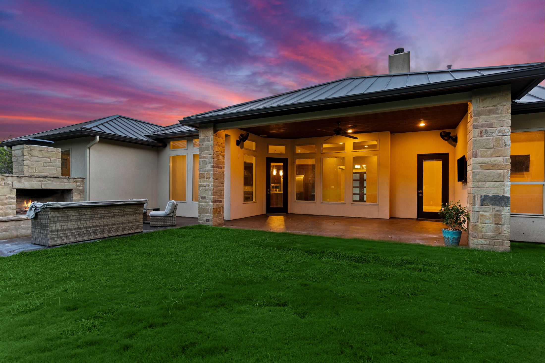 Modern home exterior at dusk with illuminated patio, stone accents, and manicured lawn