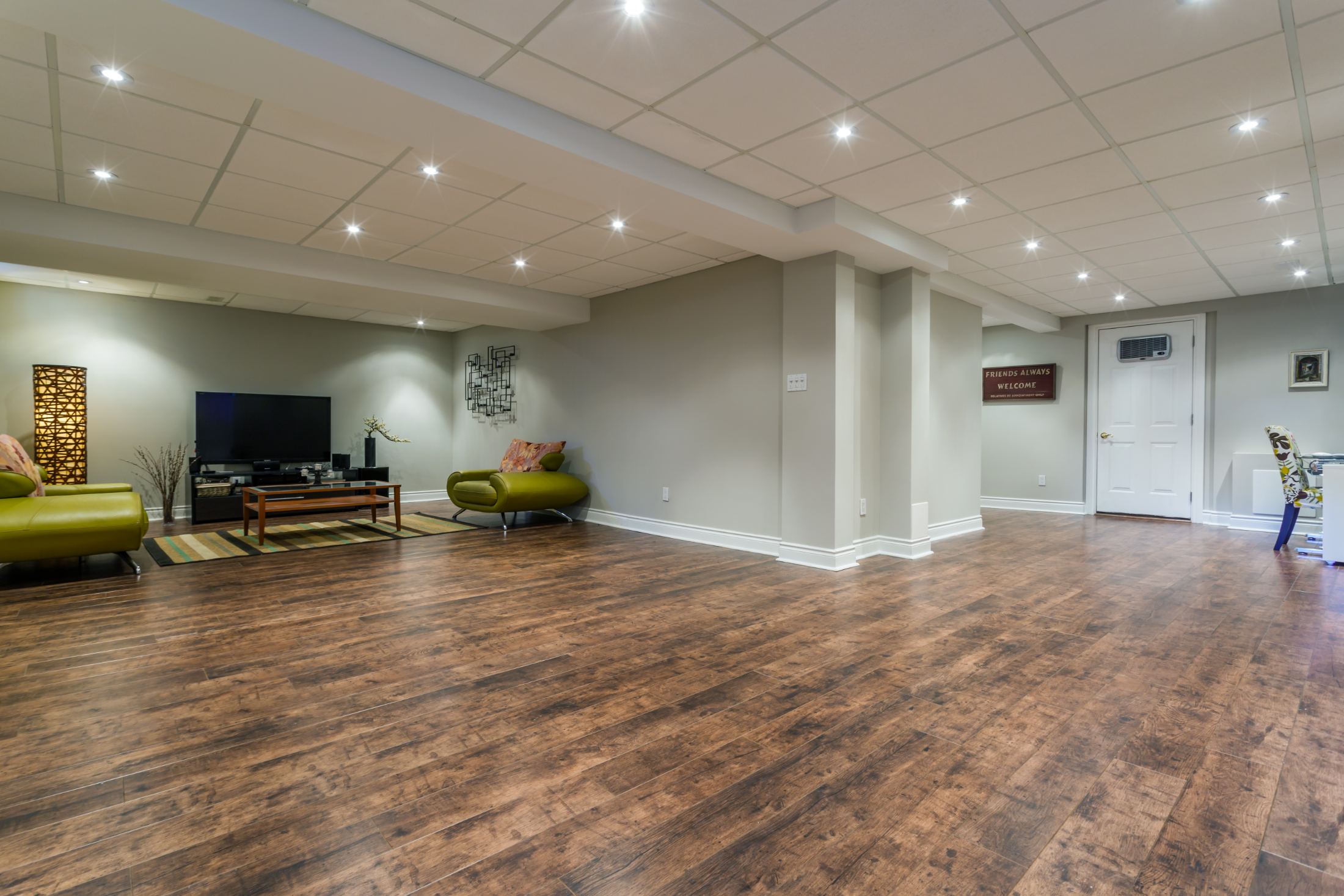 Spacious finished basement with wood flooring, recessed lighting, green chair, TV entertainment center, and white doors
