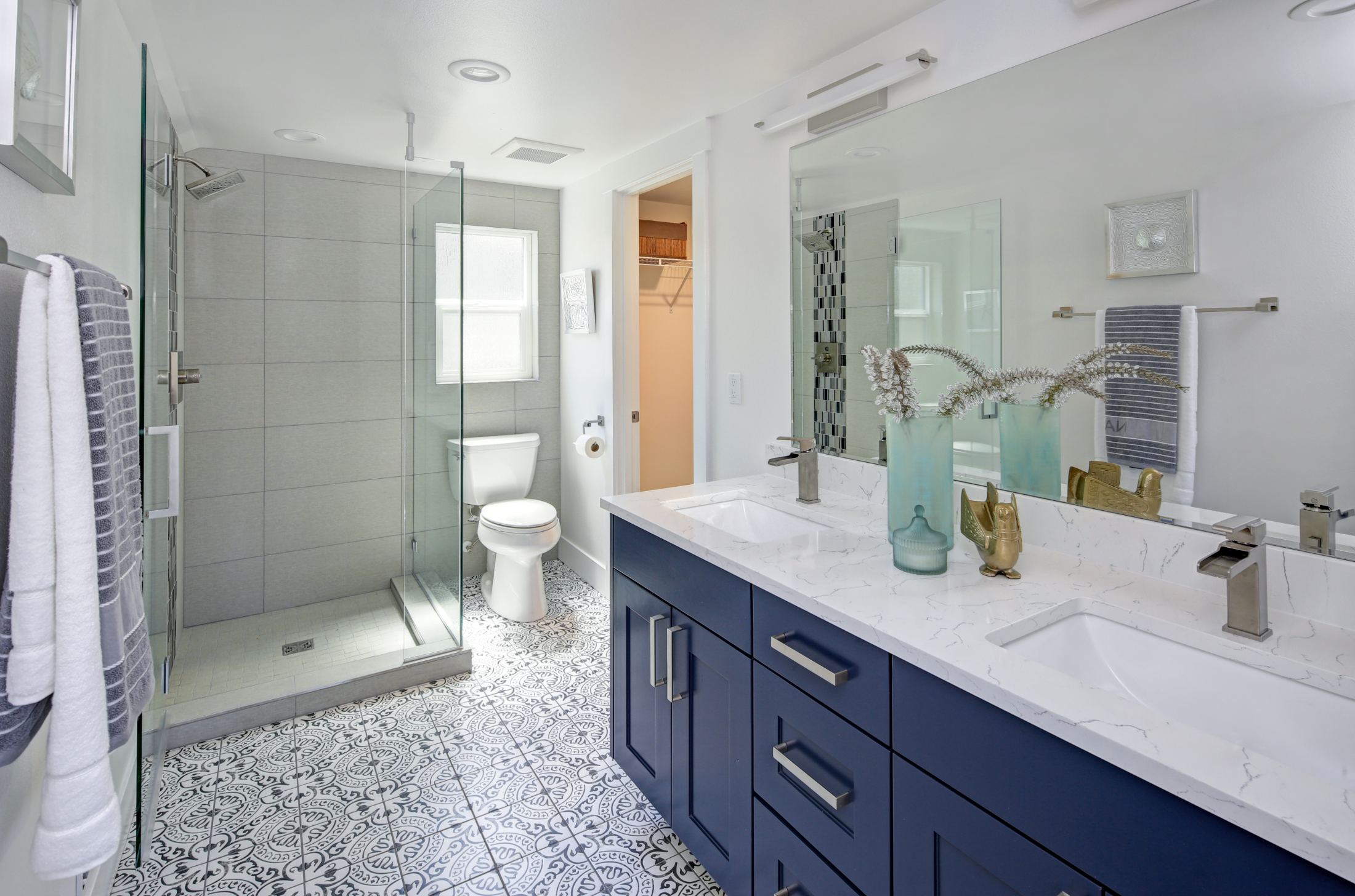 Modern bathroom with dual vanity, walk-in shower, navy cabinetry, and patterned tile flooring
