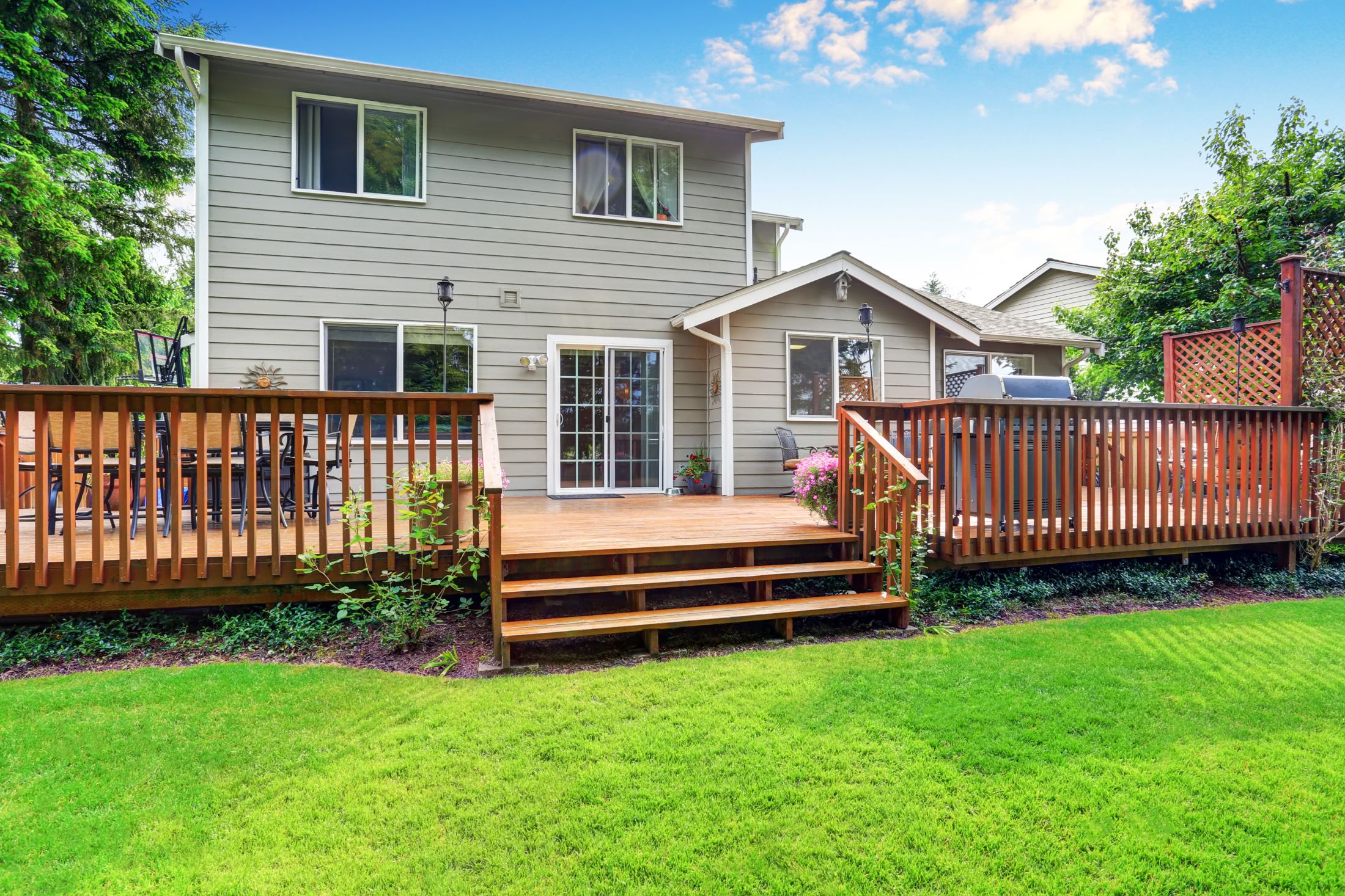Two-story house with wooden deck, railing, and manicured lawn