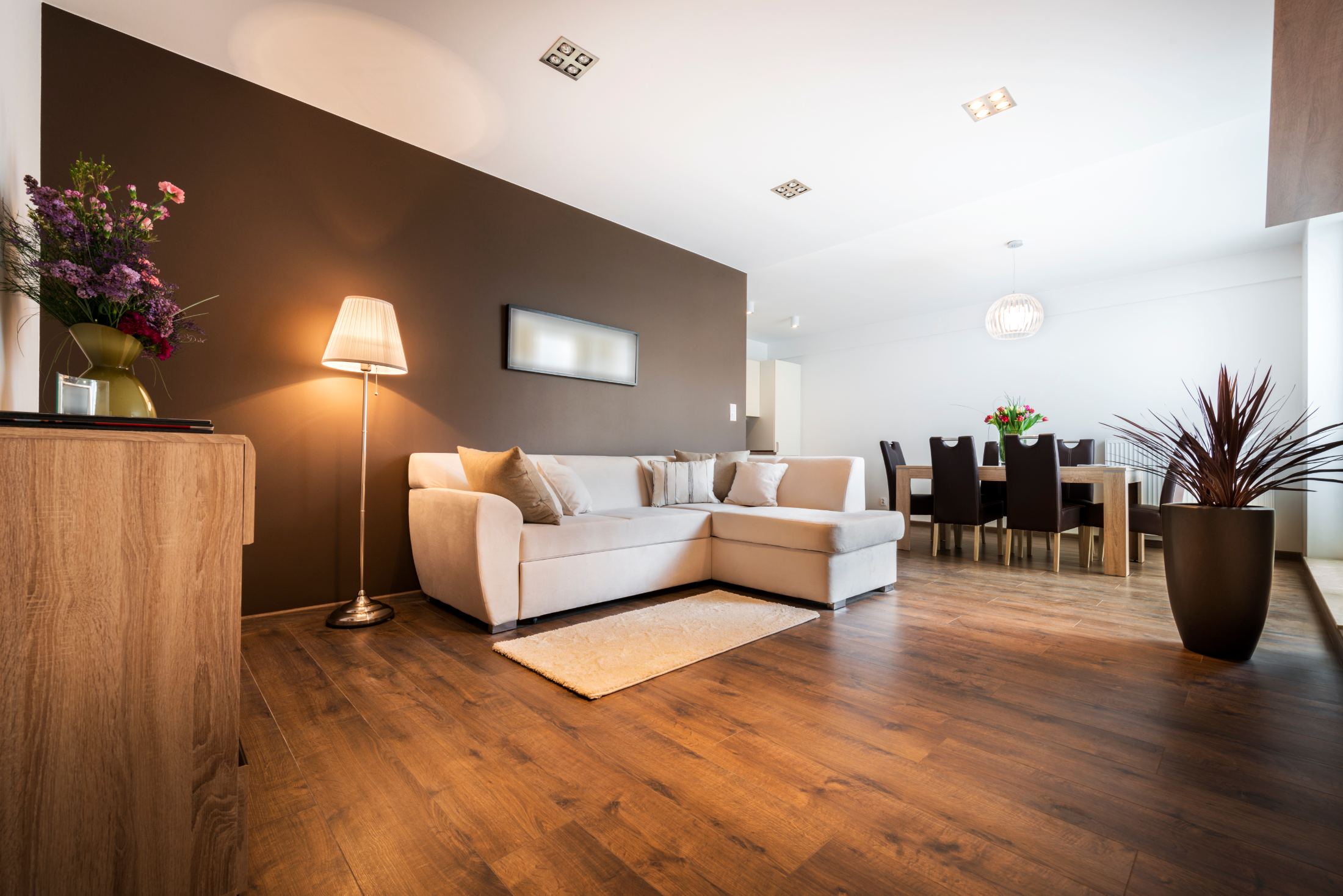 Modern living room with cream sectional sofa, brown accent wall, wooden furniture and dining area